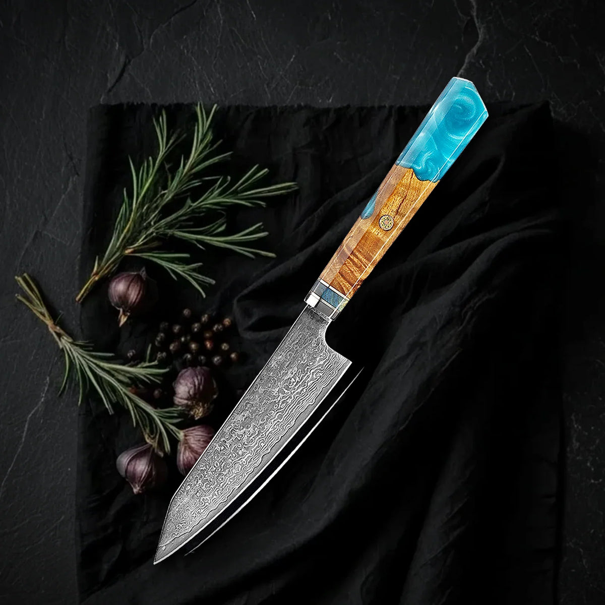 Petty Kaen 9 cm: puntilla japonesa de acero damasco con mango octogonal de resina turquesa y madera, sobre tela negra con romero