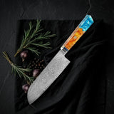 Santoku Kaen 18 cm: cuchillo multiusos japonés de acero damasco con mango octogonal de resina turquesa y madera, sobre tela negra con romero